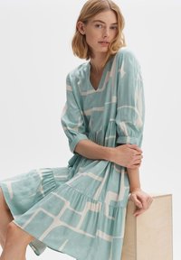 Helles blaues, gemustertes Kleid mit V-Ausschnitt, Puffärmeln und schichtweisen Rock. Hergestellt aus einem texturierten, leichten Stoff.