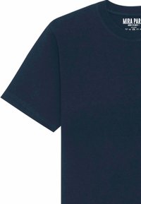 T-shirt à manches courtes bleu marine avec un col rond, fabriqué en tissu lisse. Présente une étiquette imprimée au niveau du col avec le nom de la marque et des détails.
