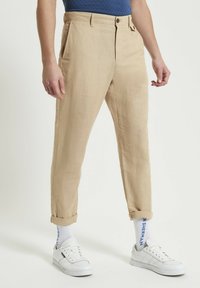Pantaloni beige in misto lino con vestibilità affusolata, dotati di tasche laterali e risvolti, abbinati a sneakers bianche e calze a righe.
