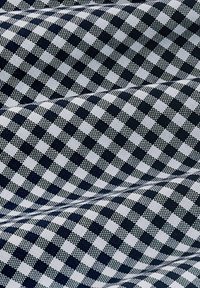 Tissu présentant un motif à carreaux bleu marin et blanc avec une texture en relief. Les carrés sont de taille uniforme, créant un design visuellement équilibré.