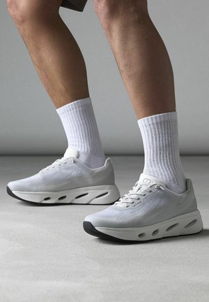 Witte sportieve schoenen met een bovenwerk van mesh, grijze accenten en een dikke zool met uitgesneden details. Gepaard met geribbelde witte sokken.