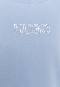 Sudadera azul claro con una tela texturizada. Presenta la inscripción blanca "HUGO" en un lugar destacado en la parte delantera. Diseño simple de cuello redondo.