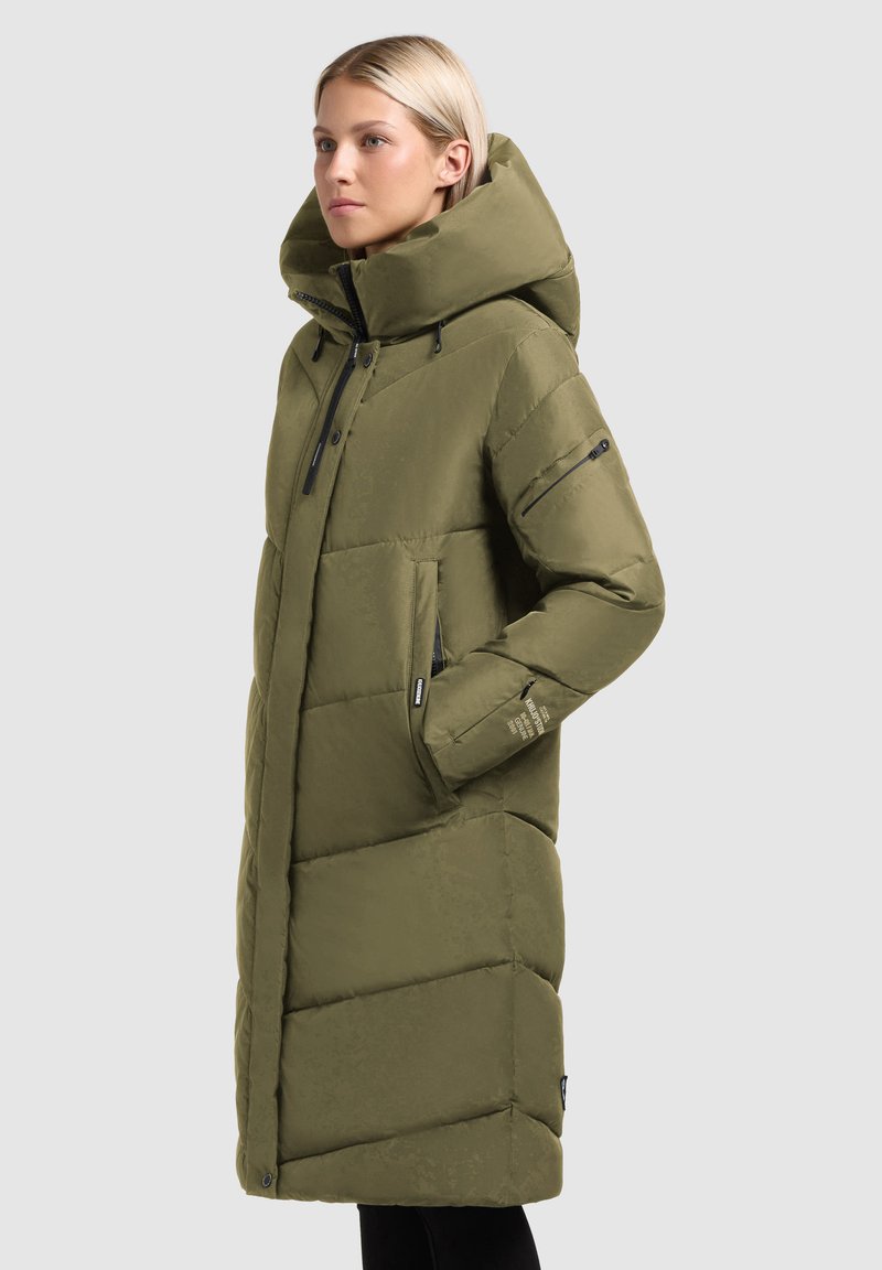 Abrigo acolchado verde oliva con un alto cuello, capucha grande y patrón de acolchado diagonal. Presenta bolsillos con cremallera y acentos de hardware negro.