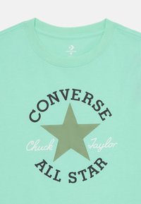 Camiseta de algodón verde menta con una gran estrella negra y el texto "CONVERSE ALL STAR" con "Chuck Taylor" en cursiva blanca debajo.