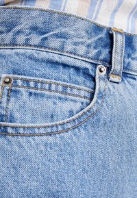 Ljusblå denimjeans med standardpassform, med orange sömmar, en bakficka och en metalldetalj i knäppningen.