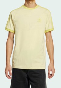 Ljusgul t-shirt med limegröna detaljer, kort ärm, och broderad logotyp. Mjuk bomullstyg, avslappnad passform, vardaglig design.