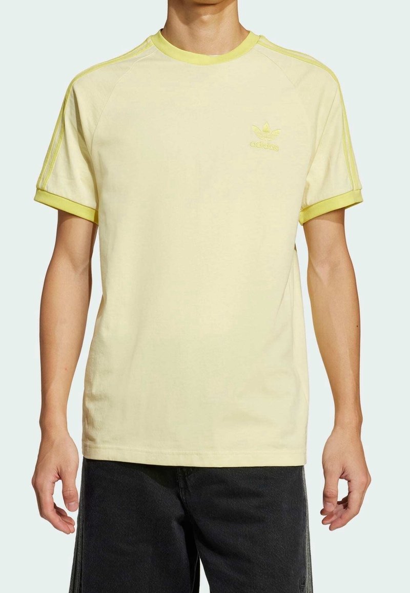 Ljusgul t-shirt med limegröna detaljer, kort ärm, och broderad logotyp. Mjuk bomullstyg, avslappnad passform, vardaglig design.