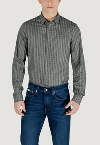 Camicia a maniche lunghe con stampa geometrica in bianco e nero, in tessuto misto cotone, colletto a camicia, abbinata a jeans in denim blu scuro.