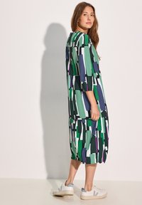 Kuosi mekko vihreänä, purppurana ja valkoisena; siinä on väljä malli, kolmasosa hihasta ja polven korkeudelle ulottuva pituus; kenkänä valkoiset lenkkarit.