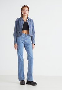 Blå texturerad kort jacka med silverknappar, tillsammans med högmidjade ljusblå jeans och svarta kraftiga plattformsskor.