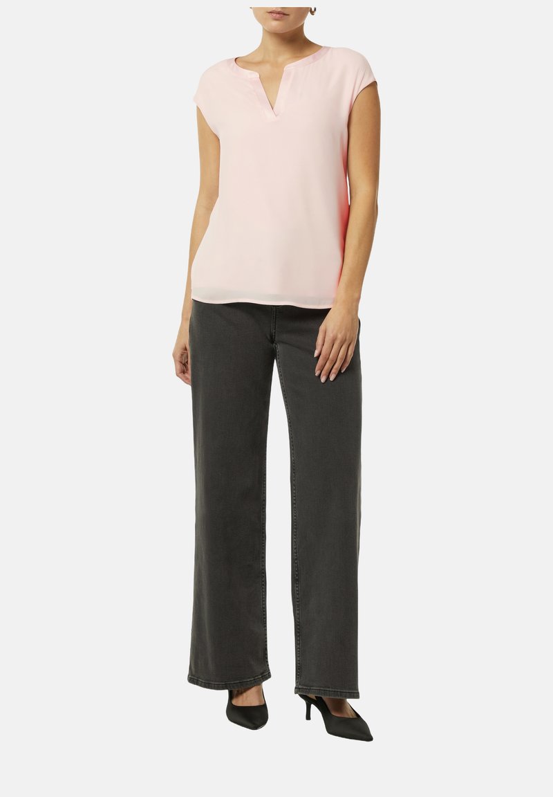 Jasnoróżowa bluzka z krótkim rękawem i dekoltem w serek o gładkiej fakturze, w połączeniu z szerokimi ciemnoszarymi dżinsami i czarnymi szpilkami.