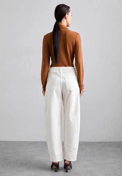 Haut long à rayures marron associé à un pantalon blanc ample taille haute et des chaussures à talons marron. Lignes épurées et design minimaliste.