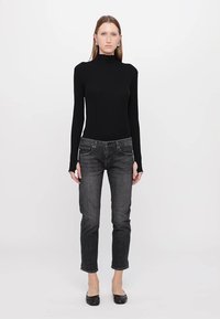 Črna dolga majica s turtleneck ovratnikom v kombinaciji s tesnimi temnimi kavbojkami. Preprost dizajn z gladko teksturo, zaključeno s klasičnim krojem.