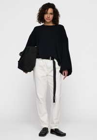 Maglietta nera a maniche lunghe con maniche larghe, pantaloni bianchi a vestibilità rilassata con cintura nera e scarpe nere slip-on. Borsa nera con tracolla.