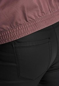 Pantalones negros ajustados con una textura suave, que cuentan con un bolsillo trasero y una cinturilla con fruncido elástico. Una blusa de color rosa claro con tela acanalada.