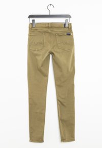 Jeans ajustados color caqui con una textura suave, cinco bolsillos, costuras en contraste y una pequeña etiqueta de la marca cerca de la cintura, colgados de una percha negra.