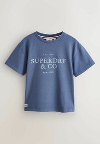 Modré tričko s krátkým rukávem s nápisem „SUPERDRY & CO NEW YORK“ vytištěným bílou barvou na přední straně, zobrazené na čistě bílém pozadí.