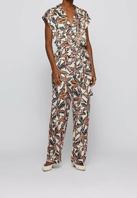 Mono floral en crema con patrones de hojas en naranja y negro, con un diseño envolvente, mangas cortas y un cinturón atado. Corte ajustado.