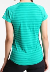 Kortärmad, figurnära träningsskjorta i teal med horisontella ränder. Tillverkad av ett slätt, lätt material och har raglanärmar.