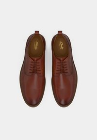Pair of polished brown leather lace-up men's dress shoes with rounded toes and branded insoles, shown from above on a white background.