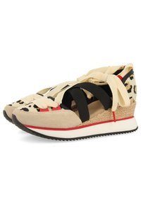 Zapatillas de ante beige con correas elásticas negras y cordones de color marrón claro. Presentan una cuña elevada con detalles rojos y una suela texturizada.