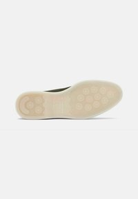 Suola delle scarpe in gomma leggera di un beige chiaro, caratterizzata da un motivo circolare e un design con grip testurizzato, etichettata con il marchio "Saknosso".