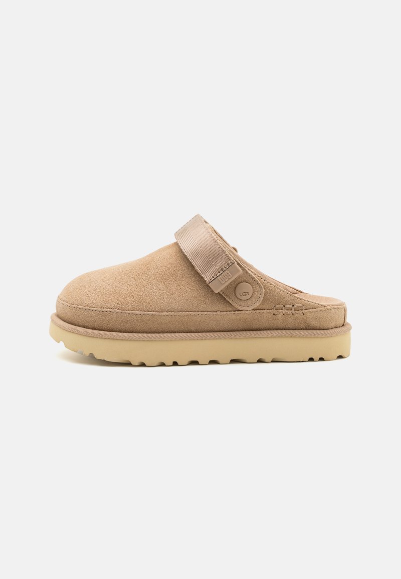 Suede slip-on clog in beige with a textured upper, adjustable strap, and a sturdy rubber sole featuring a lug pattern for grip.
