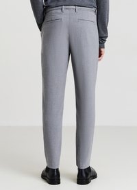Pantaloni grigi chiari in tessuto testurizzato, design slim fit, due tasche posteriori e abbinate a scarpe nere.