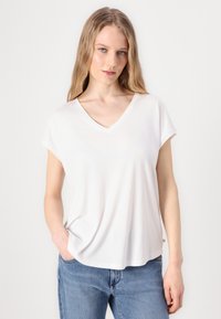 Hvit v-hals t-skjorte med korte rullede ermer, laget av glatt stoff, med en løs passform og detaljer i sidesømmen. Kombinert med blå jeans.