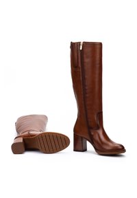 Bottes en cuir marron jusqu'au genou avec fermeture éclair latérale et talon carré, une botte debout et l'autre montrant une semelle à motifs.
