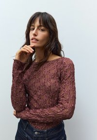 Bordeaux kant top met lange mouwen, voorzien van een bloemenpatroon en een transparante textuur, gecombineerd met donkere denim jeans, met de nadruk op de ingewikkelde details.