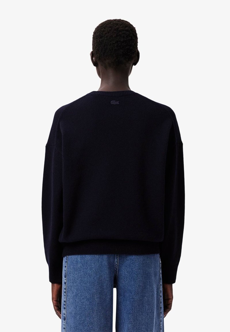 Marineblauer, oversized Pullover aus weichem Material, mit Rundhalsausschnitt und gerippten Bündchen. Lacoste-Logo auf der Rückseite gestickt.