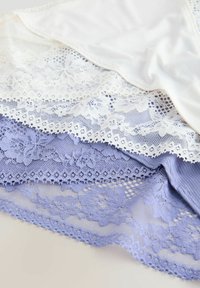 Couches de tissu en dentelle délicate en blanc et lavande avec des motifs floraux et des bords festonnés sur un fond clair.