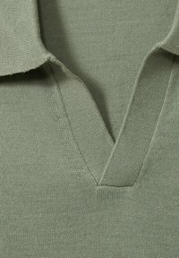 Zbliżenie na zielony kołnierz koszulki polo z dzianiny z dekoltem w kształcie litery V oraz widoczną strukturą dzianiny.