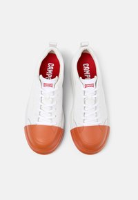 White sneakers with a rubber orange toe cap, flat laces, and red insoles. The brand "Camper" is printed on the tongue and insoles.