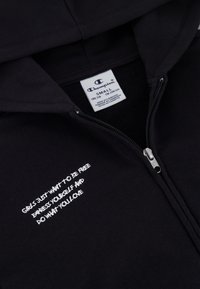 Felpa nera con zip realizzata in tessuto morbido. Presenta una scritta ricamata bianca, "LE RAGAZZE VOGLIONO SOLO ESSERE LIBERE," vicino alla zip. Etichetta Champion all'interno.