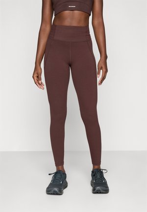 High-waisted brown leggings made from stretchy fabric, featuring seam details and a smooth finish, paired with dark athletic shoes.