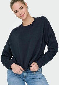 Sweat-shirt bleu marine avec un col rond, des manches longues et une coupe décontractée. Texture douce. Associé à un jean bleu clair.