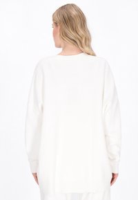Übergroßer weißer Strickpullover mit langen Ärmeln, gerippten Bündchen und rundem Saum. Glatte Textur und lockere Passform.