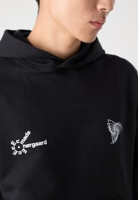 Hoodie noir avec cordon de serrage, arborant du texte imprimé blanc et des graphismes sur le devant. Texture de tissu douce, coupe décontractée.