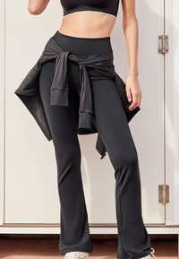 Leggings noires évasées en tissu extensible, associées à une veste noire nouée. Le design présente une texture lisse et une coupe ajustée.