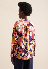 Camicia a maniche lunghe con un motivo floreale colorato in rosa, giallo e blu navy su uno sfondo crema; tessuto morbido con una vestibilità rilassata.