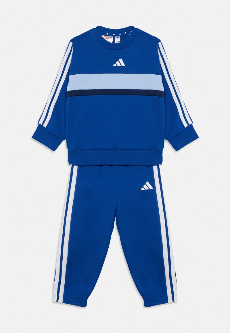 Súprava modrej športovej mikiny a nohavíc. Mikina má svetlomodrý pás a biele pruhy Adidas. Nohavice majú zhodné pruhy a logo.