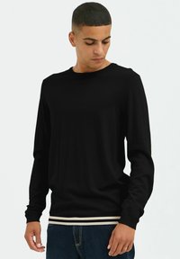 Maglietta nera a maniche lunghe con collo tondo, caratterizzata da una texture a maglia a coste e un orlo a strisce contrastanti in vita.