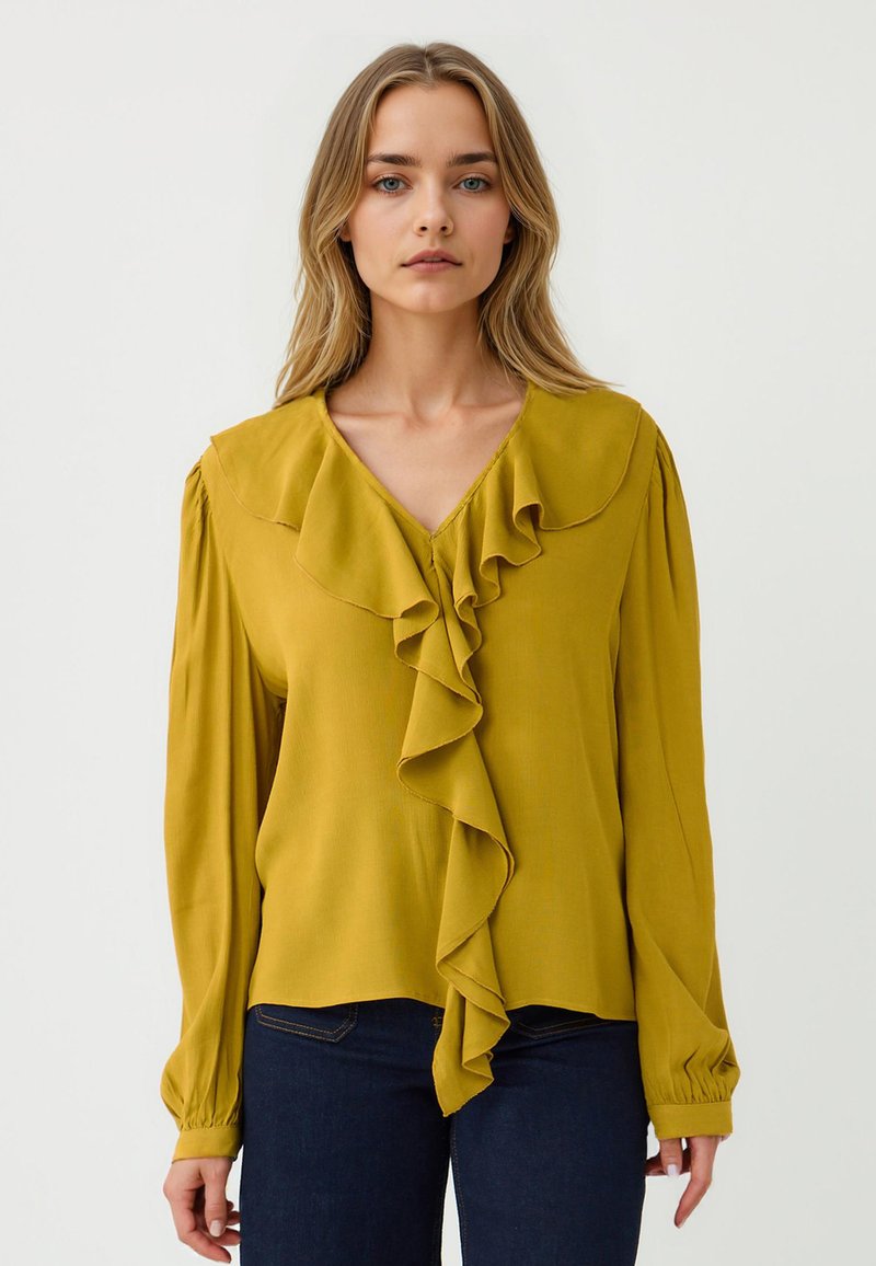 Blusa gialla senape con maniche lunghe, dettagli in rouches lungo il davanti, scollatura a V e polsini elasticizzati. Tessuto morbido e leggero.