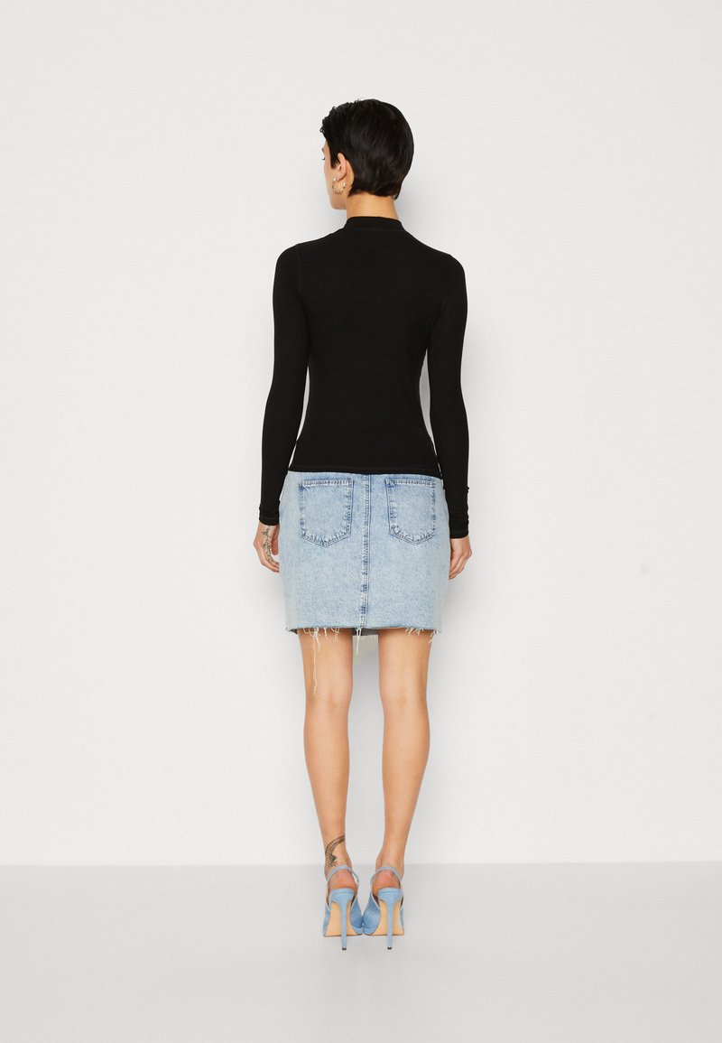 Schwarzes Langarmoberteil kombiniert mit einem hellblauen Jeans-Minikleid mit fransigen Kanten. Hellblaue High Heels runden das Outfit ab.