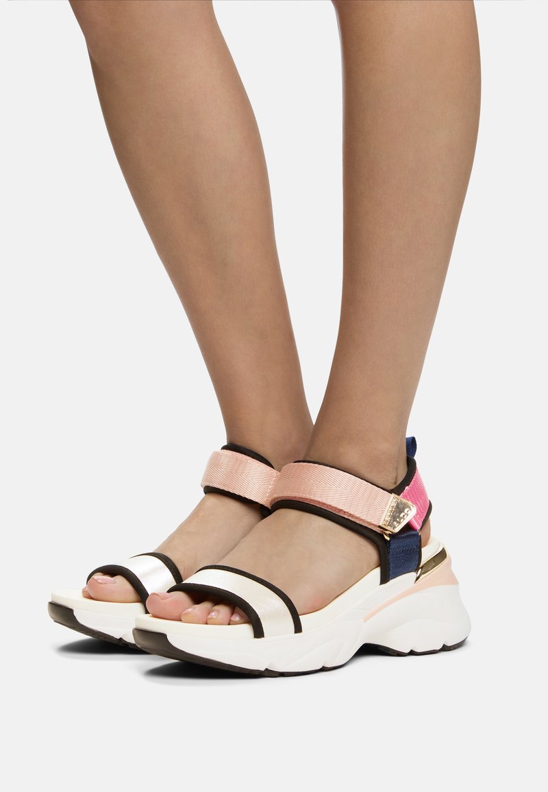 Sandali bicolore con una fascia bianca lucida sulla punta, bordi neri a contrasto e cinturini elastici rosa e blu. Suola bianca spessa.