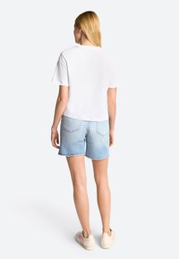 White cropped t-shirt with a round neckline, paired with light blue denim shorts featuring frayed edges and two back pockets.