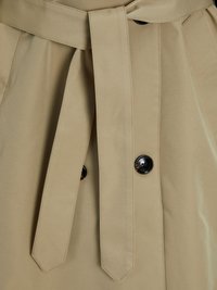 Beiger Trenchcoat-Stoff mit gebundenem Gürtel, ausgestattet mit schwarzen Knöpfen und vertikalen Falten. Glatte Textur und taillierter Schnitt mit sichtbaren Nähten.