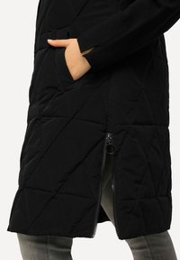 Mustat topatut takit, joissa on vetoketjullinen sivu, timanttikuosiset ja neulottu hihat. Sisältää sivutaskun, valmistettu kevyestä kankaasta.